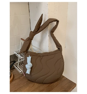 Close-up of brown quilted croissant bag with wave stitching and blue knot charm