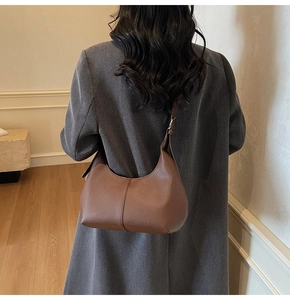 Detail of dark brown lychee leather texture and curved seam on hobo bag with wide strap