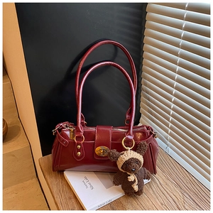 Close-up of retro burgundy leather boston bag with vintage rivets and a brown knit bear charm