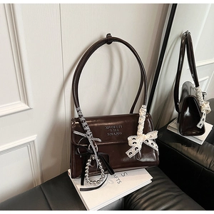 Close-up of brown glossy shoulder bag with lace bow and silver bead chain details