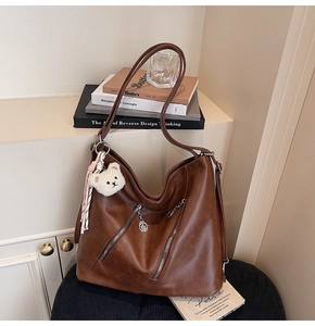 Détail d'un sac cabas en cuir marron avec fermetures éclair et un ours en peluche