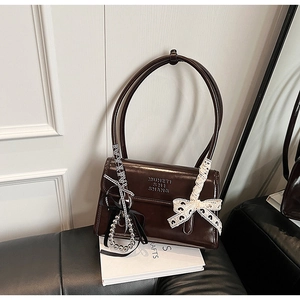 Close-up of a chocolate brown leather shoulder bag with a lace bow and ribbon detail