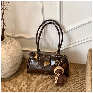 Detail of dark brown leather handbag featuring gold clasp and cute knitted bear charm