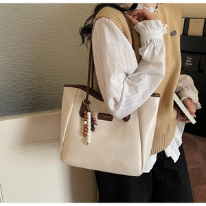 Detail of off-white tote bag with brown handles and a retro wooden bead charm accessory
