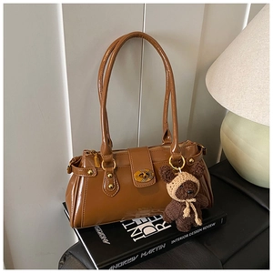 Detail of vintage brown glossy leather shoulder bag with gold hardware and plush bear charm
