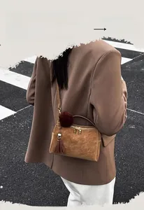 Gros plan d'un sac polochon en daim marron avec fermetures dorées et pompon bordeaux