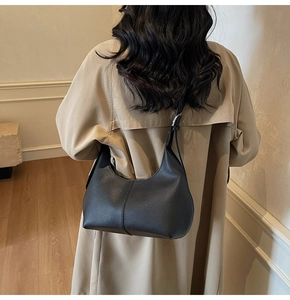 Close-up of black pebble leather hobo bag with silver hardware on a beige trench coat