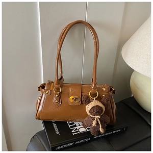 Detail of brown glossy shoulder bag with gold twist lock and a cute knit teddy bear charm