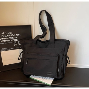 Detail of black nylon travel tote featuring a large front flap pocket and dual handles