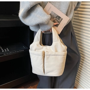 Close-up of minimalist cream tote bag featuring two front pockets and canvas texture