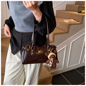 Detail of dark brown glossy patent leather bag with gold buckle and cute teddy bear charm
