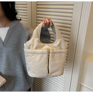 Detailed view of cream quilted tote bag with dual front pockets held by a model