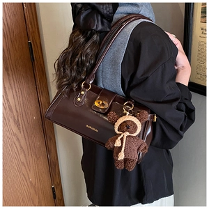 Detail of a dark brown patent leather shoulder bag with a gold lock and a knit bear charm