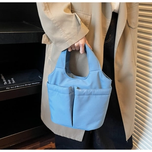 Detail of light blue fabric handbag with two front pockets and subtle woven texture