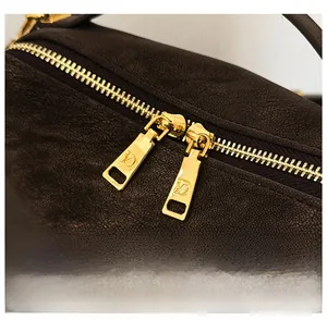 Détail de la double fermeture éclair dorée sur un sac polochon en cuir marron texturé