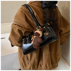 Detail of black patent leather shoulder bag with gold hardware and bear charm on model