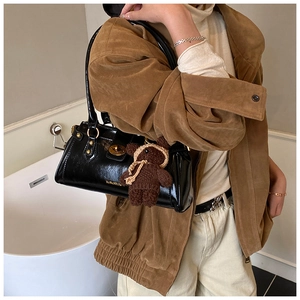 Close-up of black glossy shoulder bag with gold hardware and brown knit bear charm