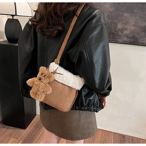 Detalle de bolso bandolera de ante marrón con ribete de lana blanca y un colgante de oso