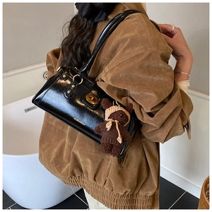 Detail of black patent leather shoulder bag featuring metal lock and plush bear charm