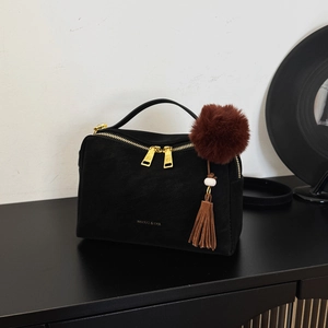 Détail d'un sac à main en daim noir avec logo doré et pendentif pompon marron