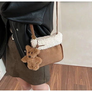 Detalle de bolso bandolera de ante marrón con ribete de vellón y colgante de osito peluche