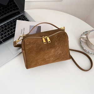 Détail d'un sac bandoulière en cuir marron texturé avec deux fermetures dorées sur table