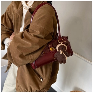 Detail of burgundy glossy leather shoulder bag featuring gold clasp and cute bear charm