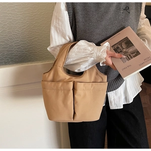 Close-up of a khaki canvas tote bag with large front pockets held by a model