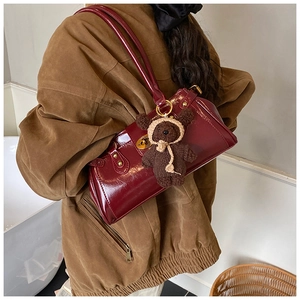Detail of dark red leather shoulder bag with gold hardware and brown bear charm