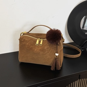 Détail d'un sac cabas en daim marron avec garniture dorée, pompon à franges et boule peluche