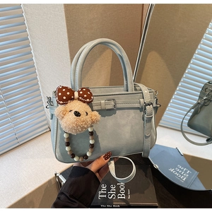 Détail du sac à main en cuir bleu gris avec pendentif ours et bandoulière sur table
