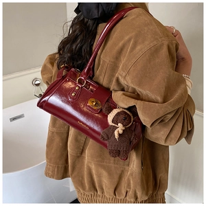 Detailed side view of dark red patent leather shoulder bag with gold hardware and bear charm