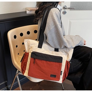 Detail of a tricolor tote bag featuring a front zipper pocket and drawstring side pockets