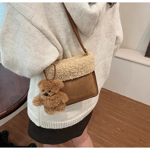 Detalle de bolso bandolera de ante marrón con ribete de felpa y amuleto de oso