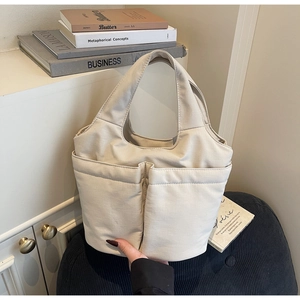 Close-up of cream canvas tote bag showing two spacious front pockets and wide handles