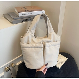 Close-up of beige canvas tote bag with front pockets and wide handles in a cozy setting
