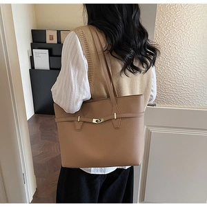 Detail of khaki tote bag with litchi texture and gold buckle on a model shoulder