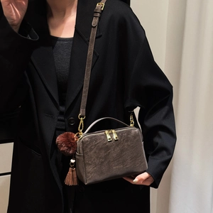 Détail du sac à bandoulière marron foncé avec fermeture éclair dorée et pompon doux