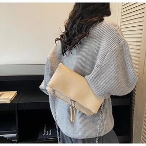 Detail of a beige lychee leather crossbody bag with silver chain strap worn by a model