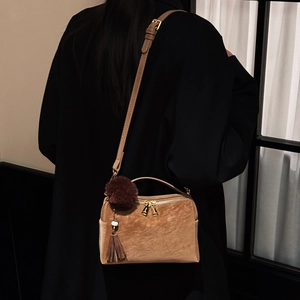 Détail du sac bandoulière en daim marron avec pompon et gland sur un manteau noir élégant