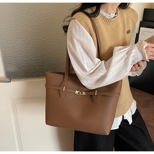 Close-up of brown litchi leather tote bag with gold metal buckle and long shoulder strap