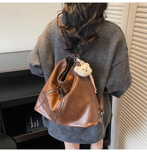 Détail du sac en cuir marron avec fermeture éclair argentée et ours en peluche