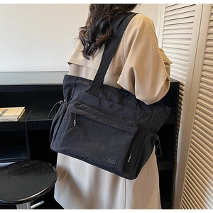 Close-up of black nylon travel tote bag worn by a model in a modern minimalist setting