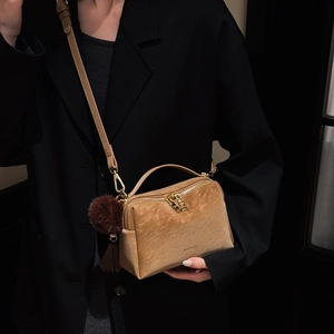 Détail du sac polochon en daim marron clair avec garniture dorée et pompon décoratif