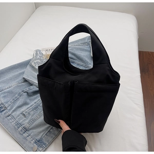 Detail of black nylon tote bag featuring spacious front pockets and reinforced handles