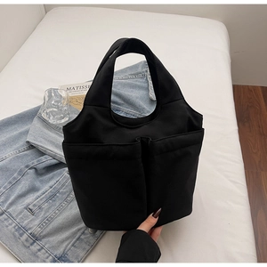 Detailed view of black tote bag with large double front pockets on white background