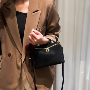 Détail d'un sac bandoulière noir avec fermeture dorée et pompon en peluche doux