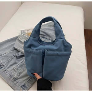 Detail of blue nylon handbag showing two large front pockets and wide sturdy handles