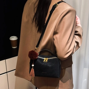 Détail du sac à bandoulière noir avec fermeture dorée et pompon décoratif en peluche rouge
