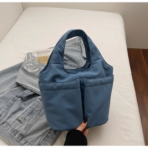 Detail shot of blue nylon handbag with front pockets, styled on a white bed sheet